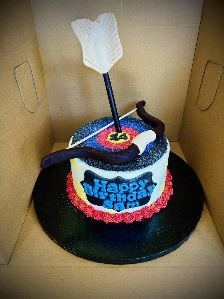 A bow and arrow target themed birthday cake that reads 'Happy Birthday Sam'