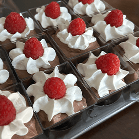A collection of min mousse cups with white frosting, topped with a raspberry